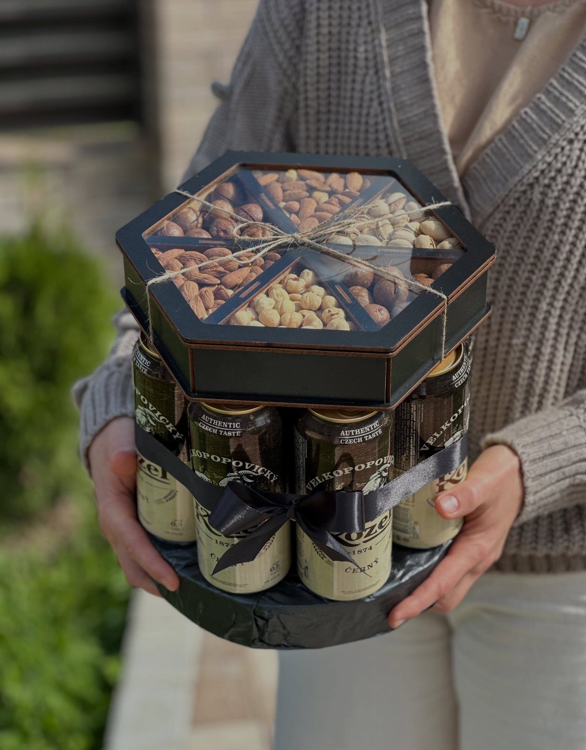 Hexagonal black gift basket with beer cans and assorted nuts held by a person