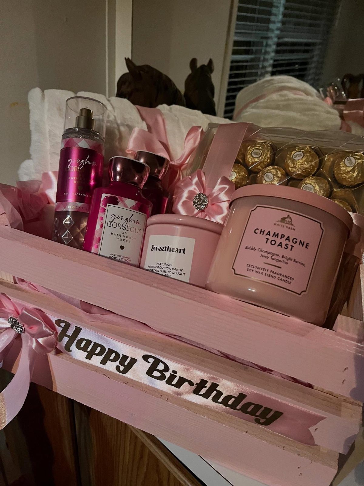 Pink birthday gift basket containing candles, perfume, chocolates, and towels in a wooden crate.