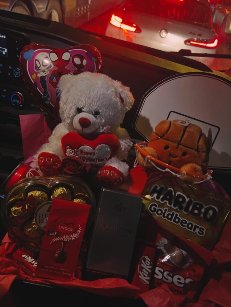 Gift basket with white teddy bear, Spider-Man balloon, and various candies in a car.