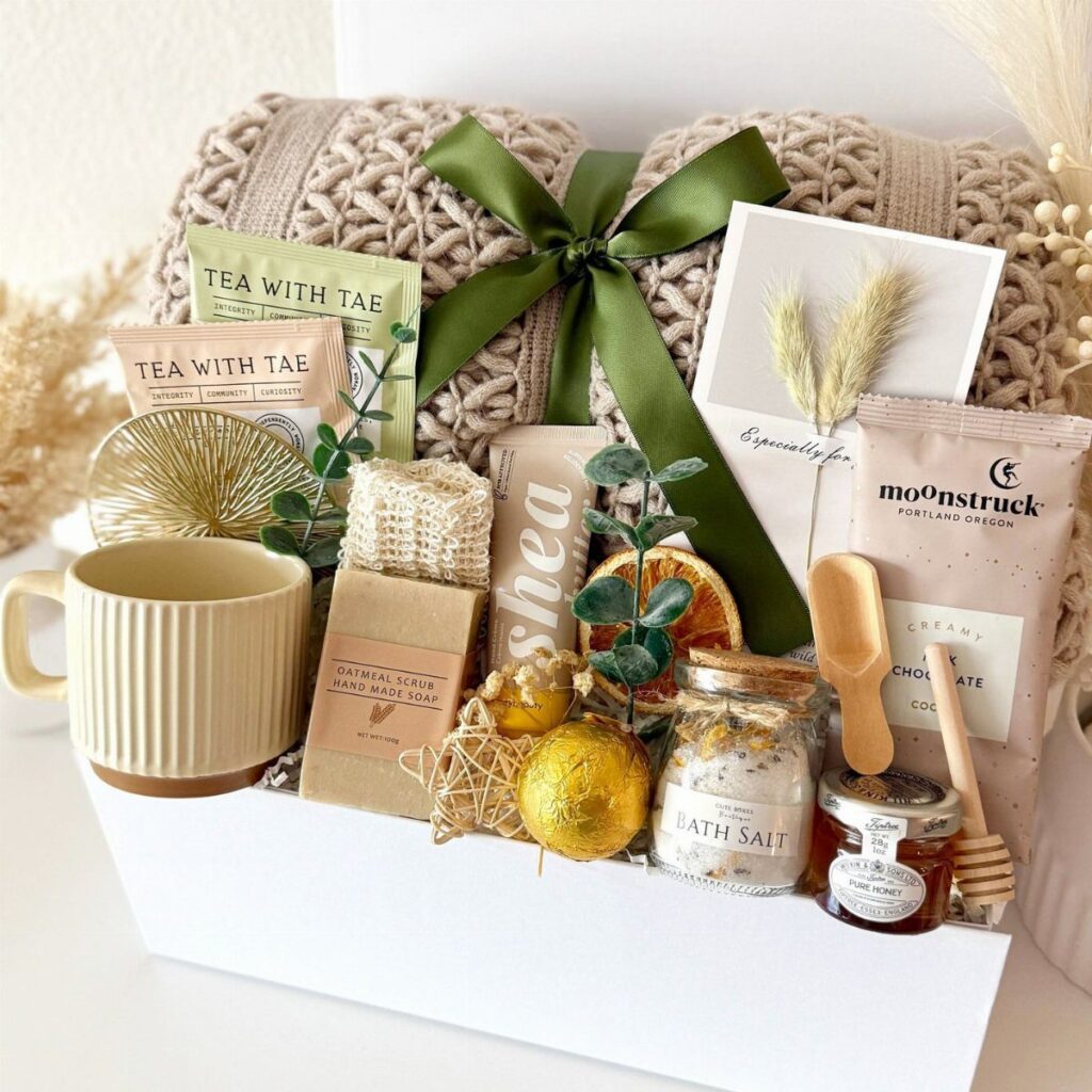 Care basket containing a knit blanket, mug, tea, and bath products in a white box.