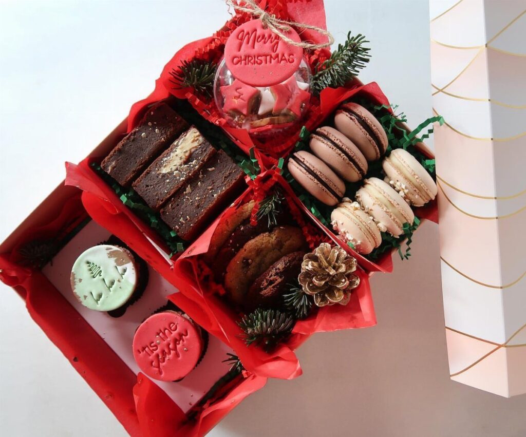 Christmas care package with brownies, macarons, cookies, and a red ornament in a box
