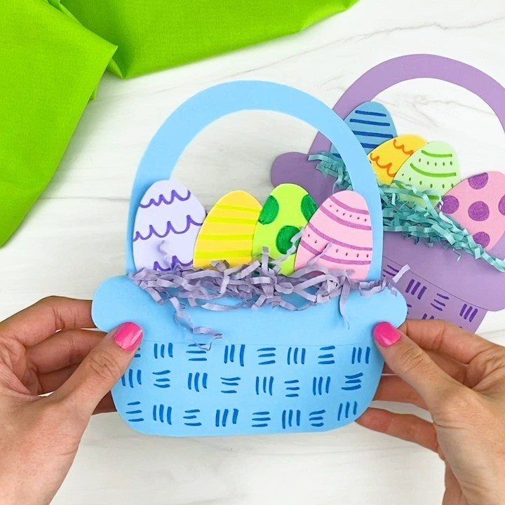 Blue paper Easter basket craft filled with colorful paper eggs and purple shred.
