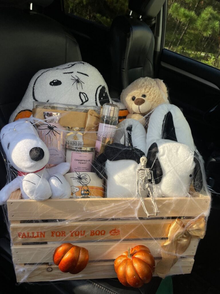 Wooden gift crate filled with Snoopy plushies, pumpkins, and autumn treats in a car.