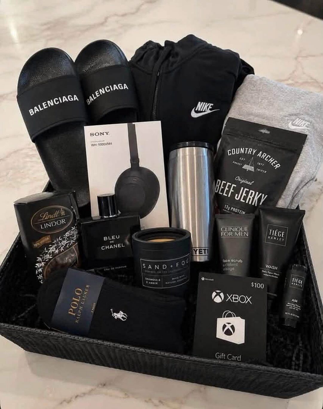 Luxury gift basket for men containing designer clothes, electronics, snacks, and grooming products.