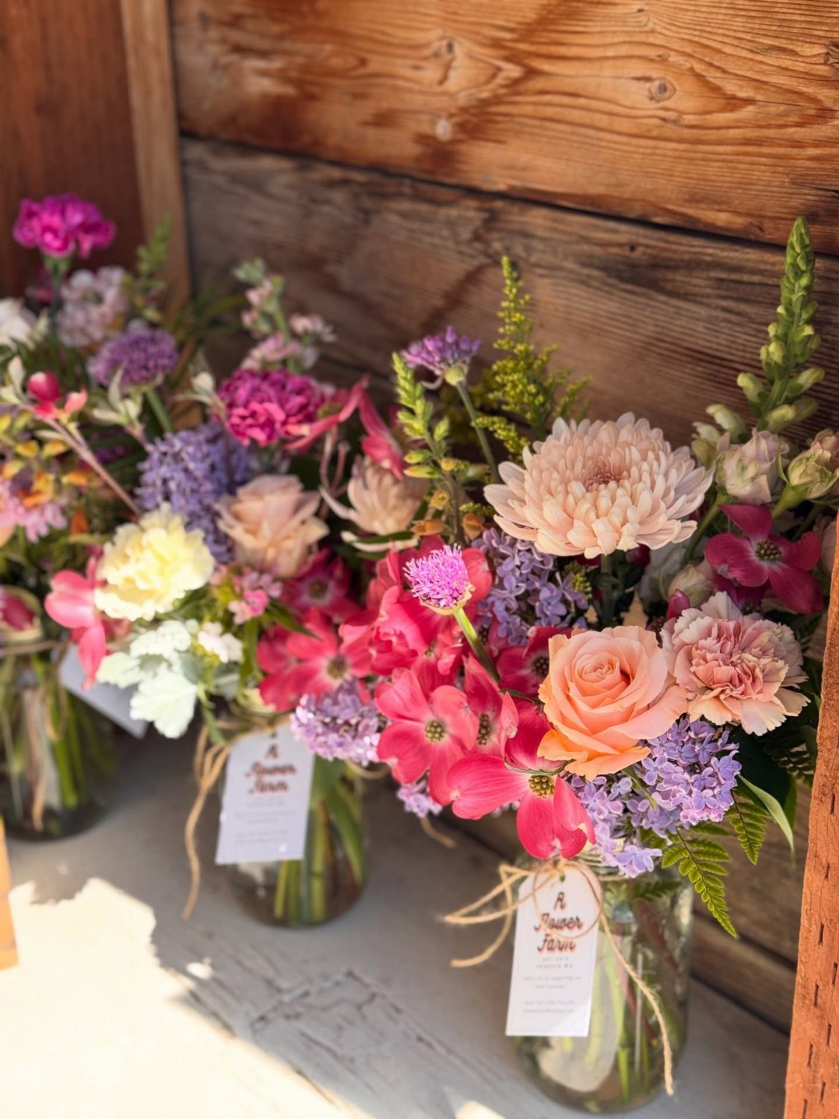 Colorful flower bouquets in mason jars tied with twine on a wooden surface.