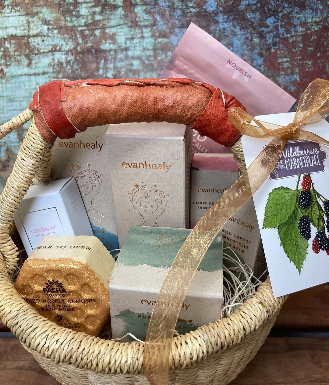 Woven gift basket filled with skincare products, a bath bomb, and a gold ribbon.