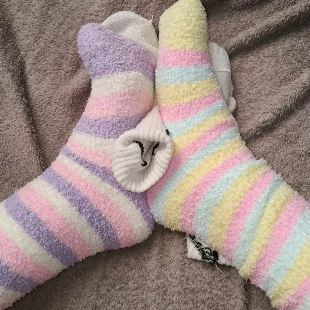 Pastel striped fuzzy socks resting on a grey textured blanket.