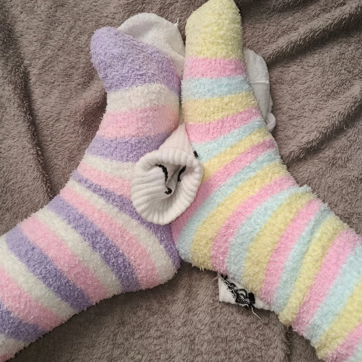 Pastel striped fuzzy socks resting on a grey textured blanket.