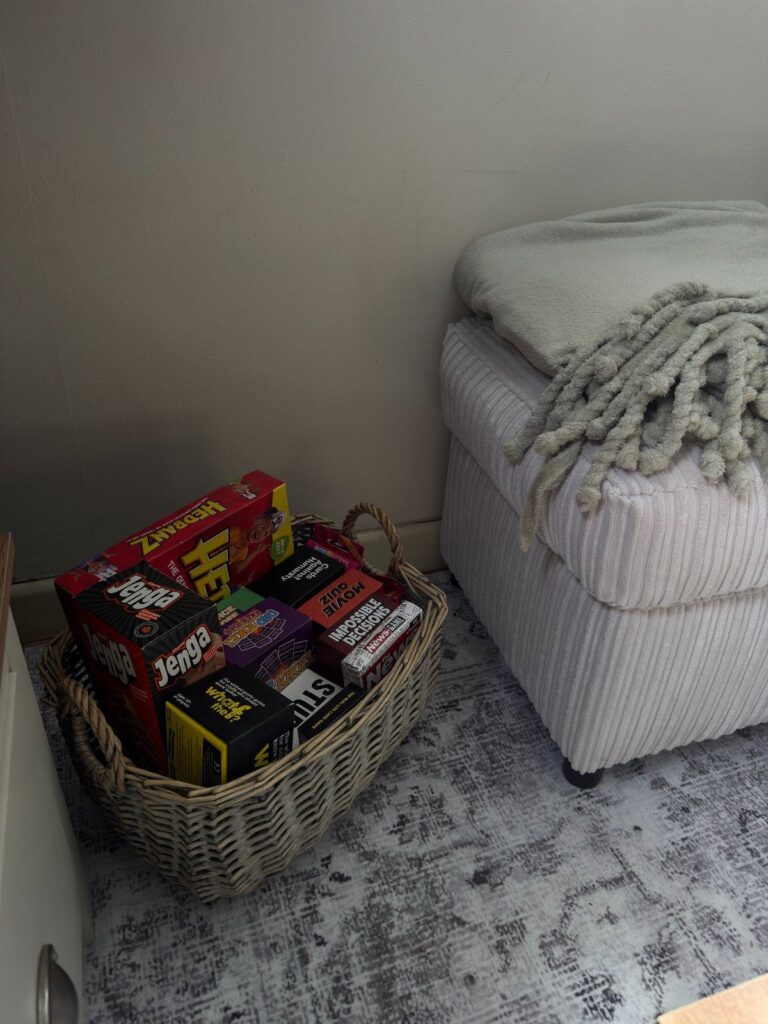 Wicker basket filled with board games sitting on a rug next to an ottoman.