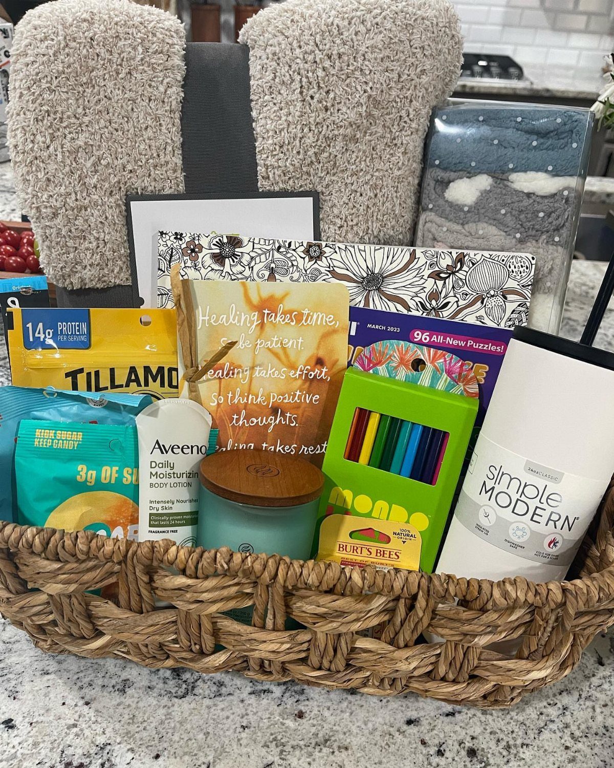 Wicker gift basket with slippers, blanket, tumbler, and snacks for recovery.