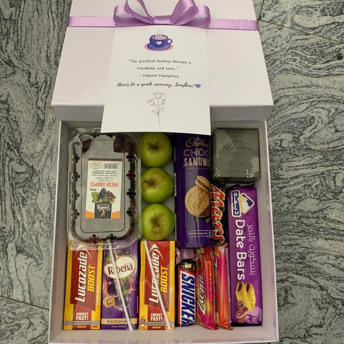 Gift box filled with fruit, energy drinks, cookies, and assorted sweet treats.