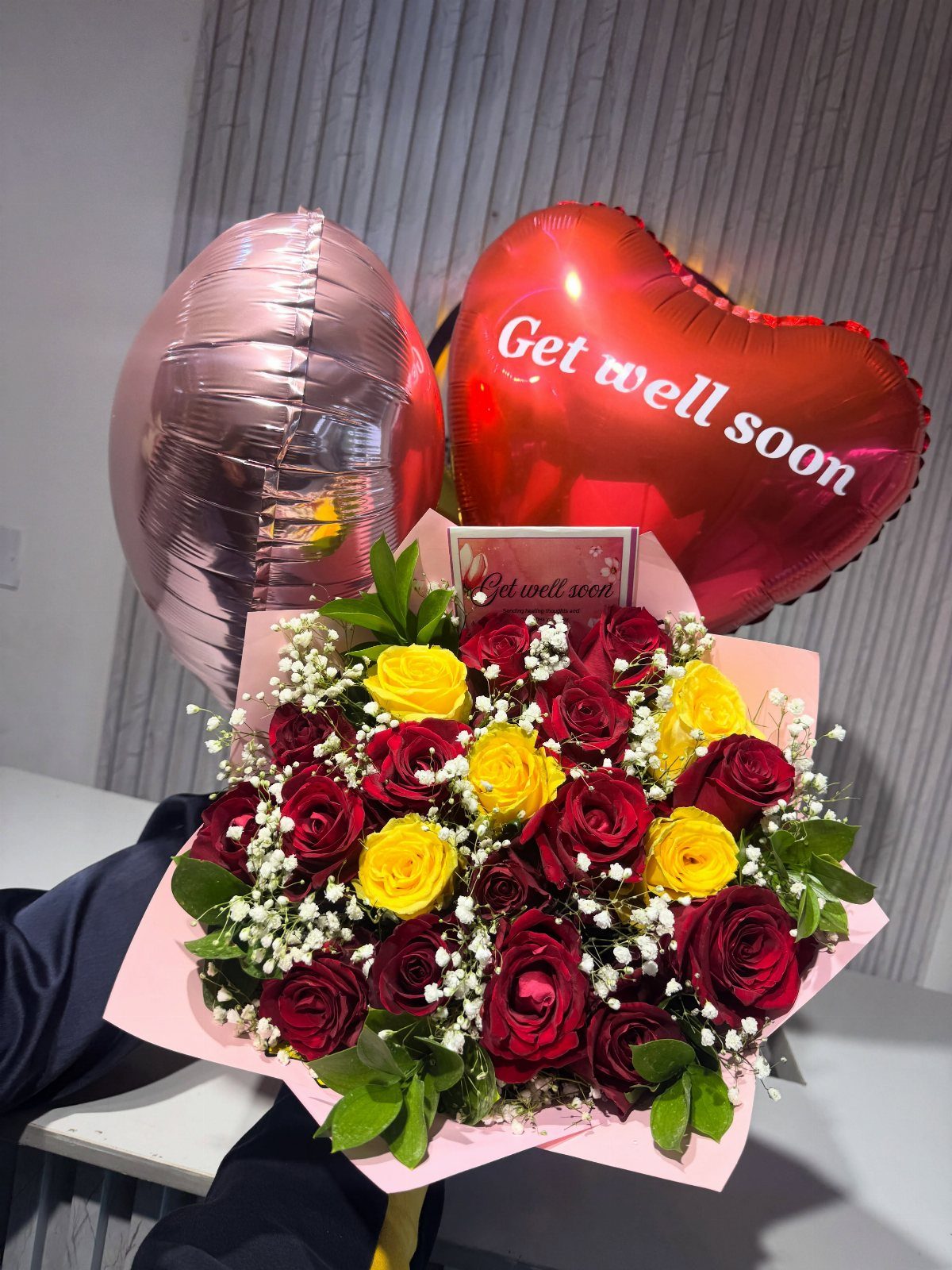 Bouquet of red and yellow roses with heart-shaped get well soon balloons.