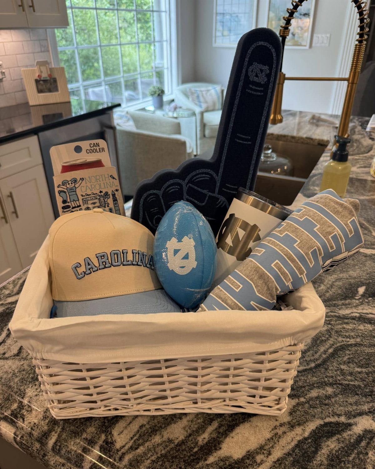 White wicker gift basket filled with blue and tan sports-themed merchandise on marble countertop