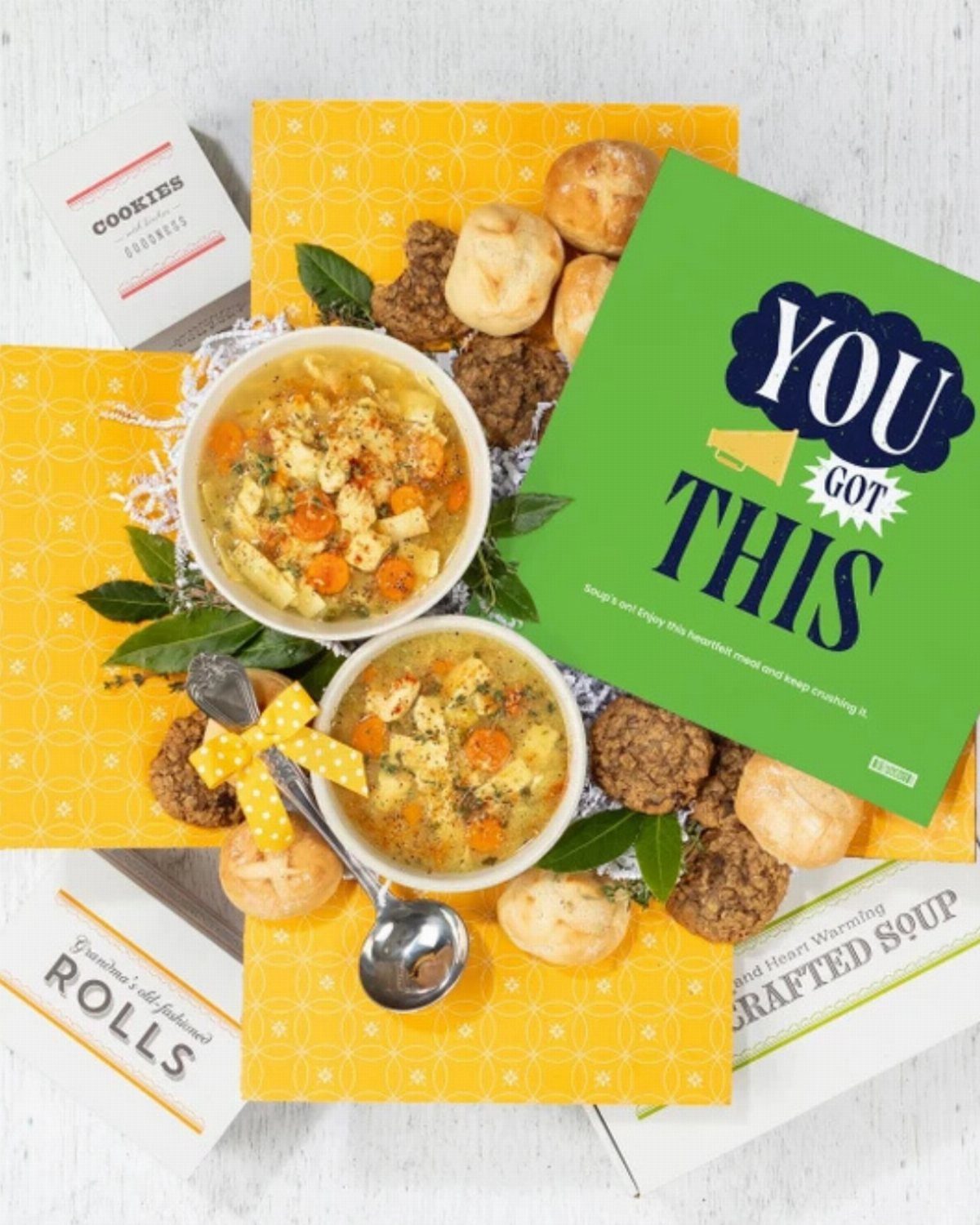 Two bowls of vegetable soup with bread rolls and cookies and a supportive card.