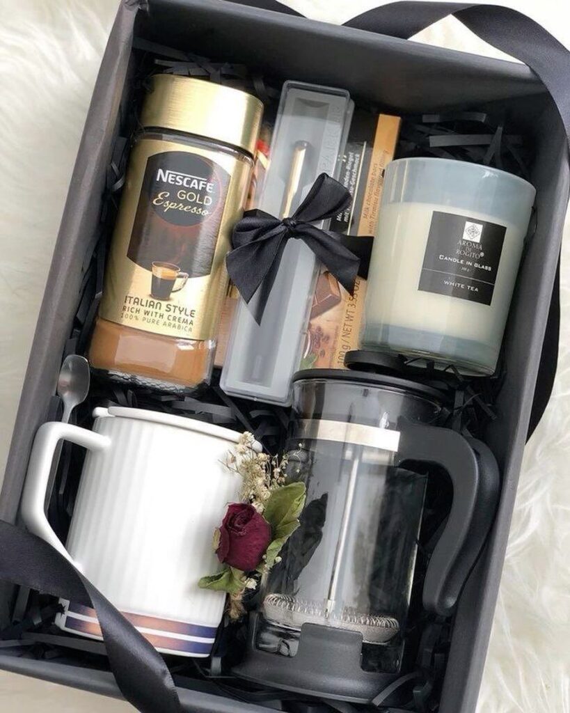 Coffee gift basket with espresso jar, French press, white mug, and scented candle.