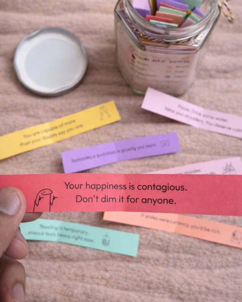 Hand holding a red positive affirmation slip from a jar of colorful notes.