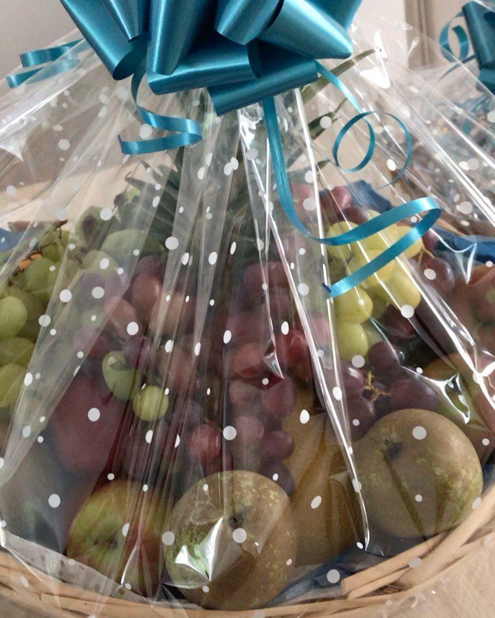 Fruit gift basket wrapped in polka dot cellophane with a blue satin bow.