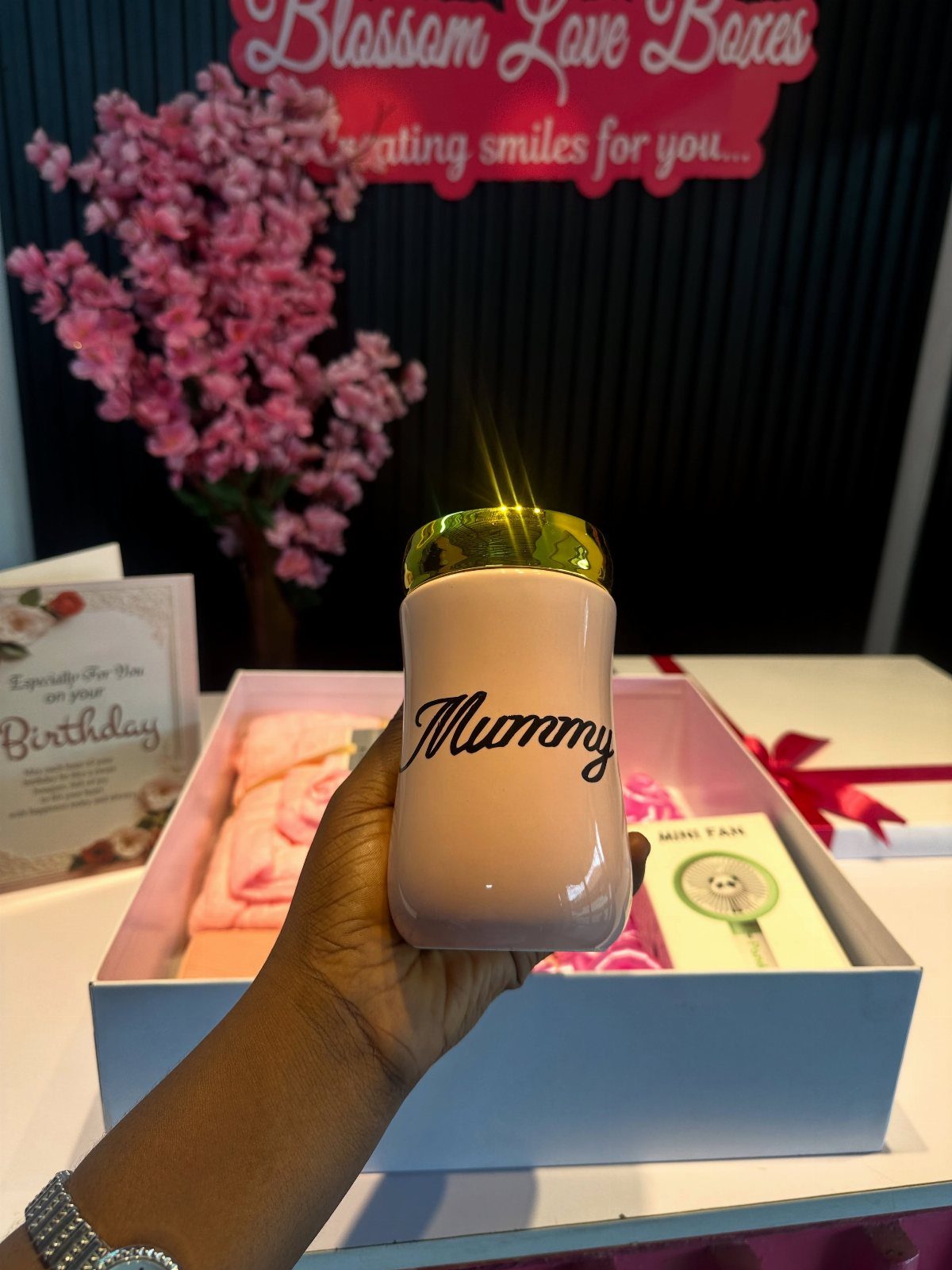 Pink Mummy tumbler held in front of a white gift box with pink contents.