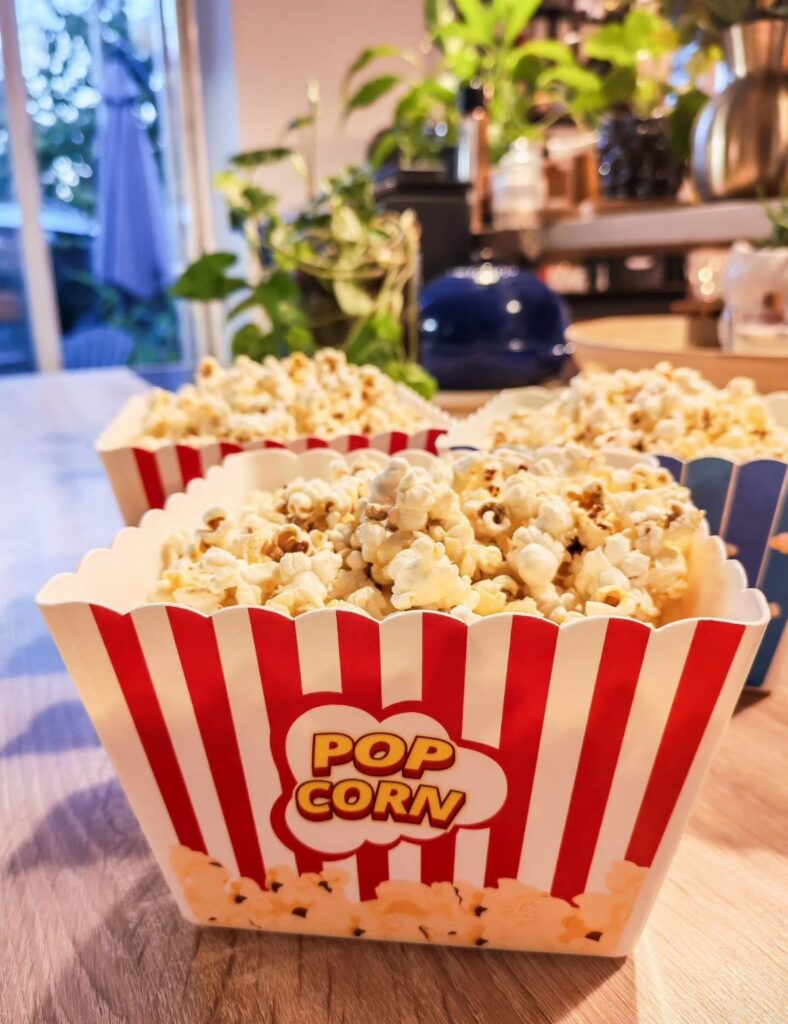Red and white striped popcorn tubs filled with popcorn on a wooden table.
