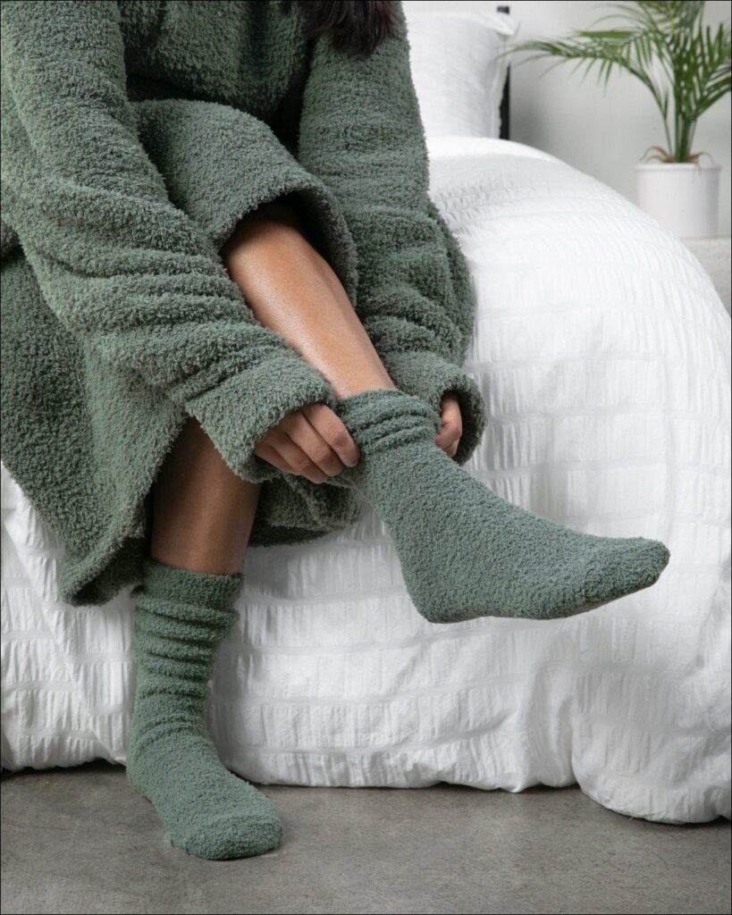 Fuzzy green socks and matching robe worn by a person sitting on a bed.
