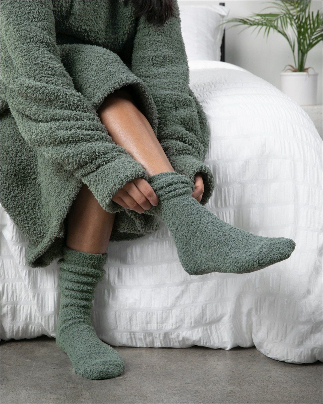 Fuzzy green socks and matching robe worn by a person sitting on a bed.