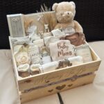 Wooden gift crate for a new mother containing a teddy bear and baby clothes.