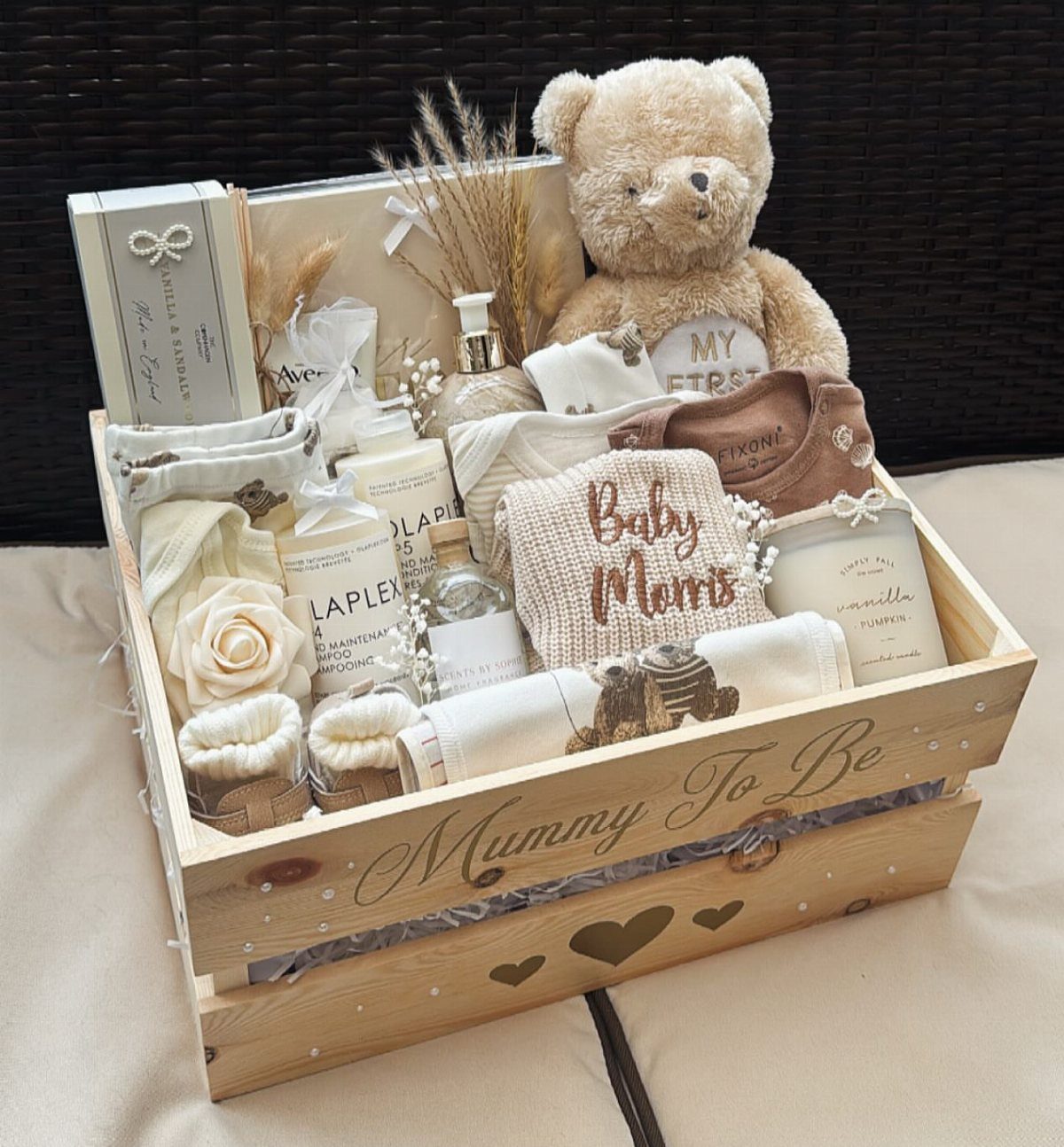 Wooden gift crate for a new mother containing a teddy bear and baby clothes.