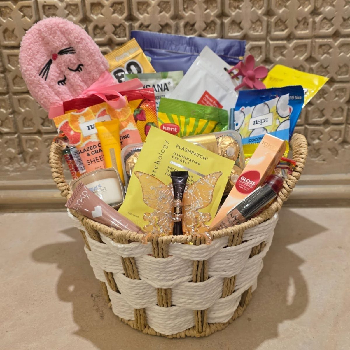 Woven gift basket filled with pink sleep mask and various skincare beauty products.