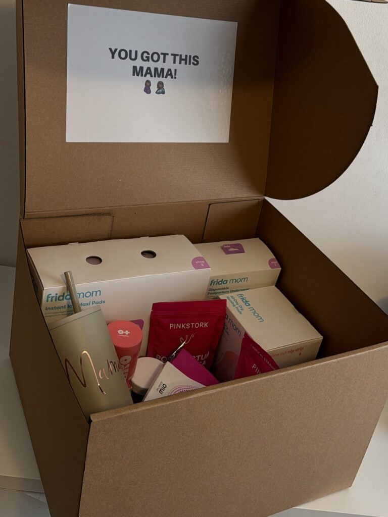 Pregnancy care package in a cardboard box with maternity products and encouraging sign.
