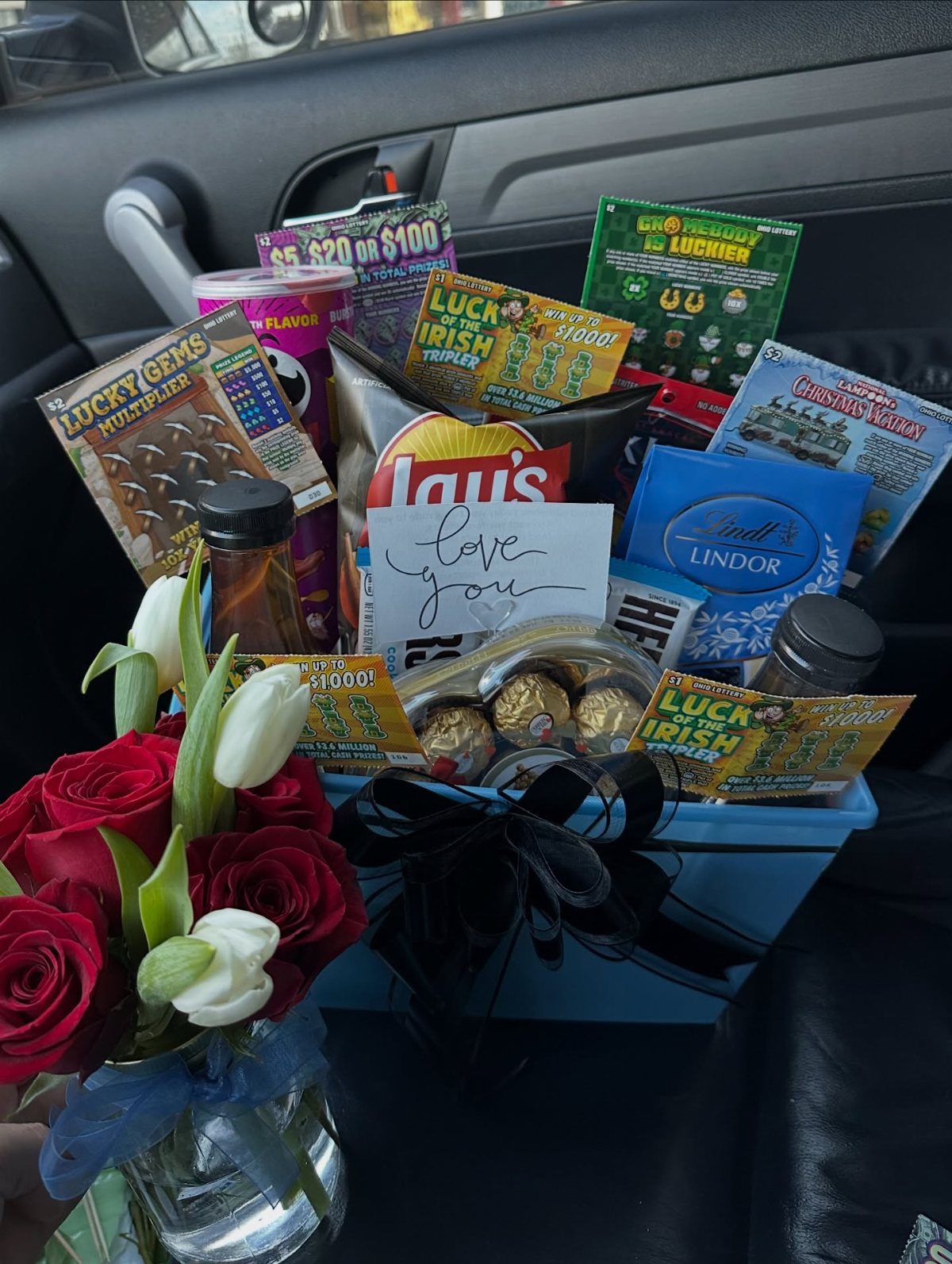 Blue gift basket filled with snacks and lottery tickets next to red roses.