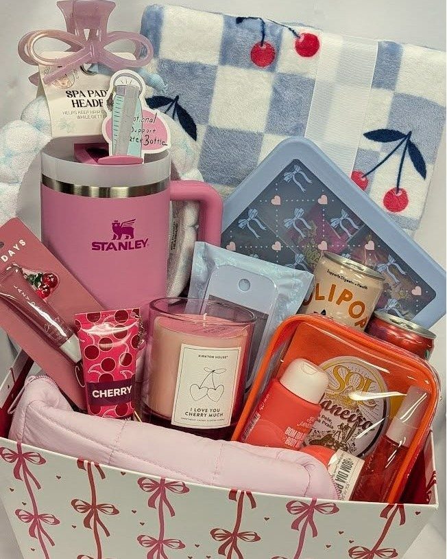 Gift basket filled with pink Stanley tumbler, cherry blanket, and beauty products.