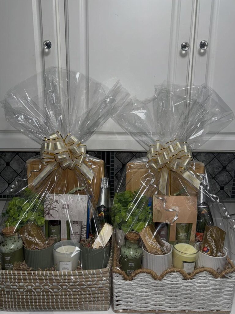 Two wrapped gift baskets containing candles and bath products with gold ribbons.