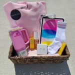 Wicker gift basket filled with pink clothing, a tumbler, and beauty products.