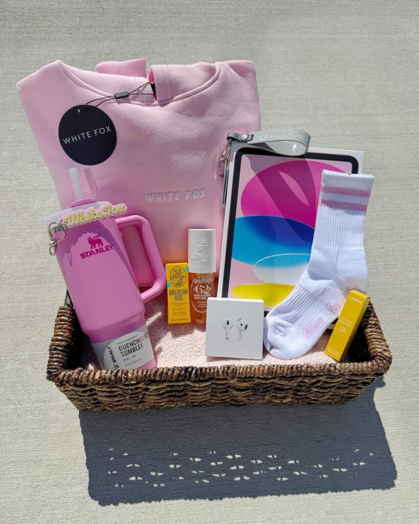 Wicker gift basket filled with pink clothing, a tumbler, and beauty products.