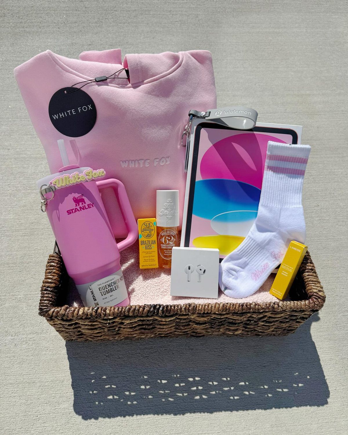 Wicker gift basket filled with pink clothing, a tumbler, and beauty products.