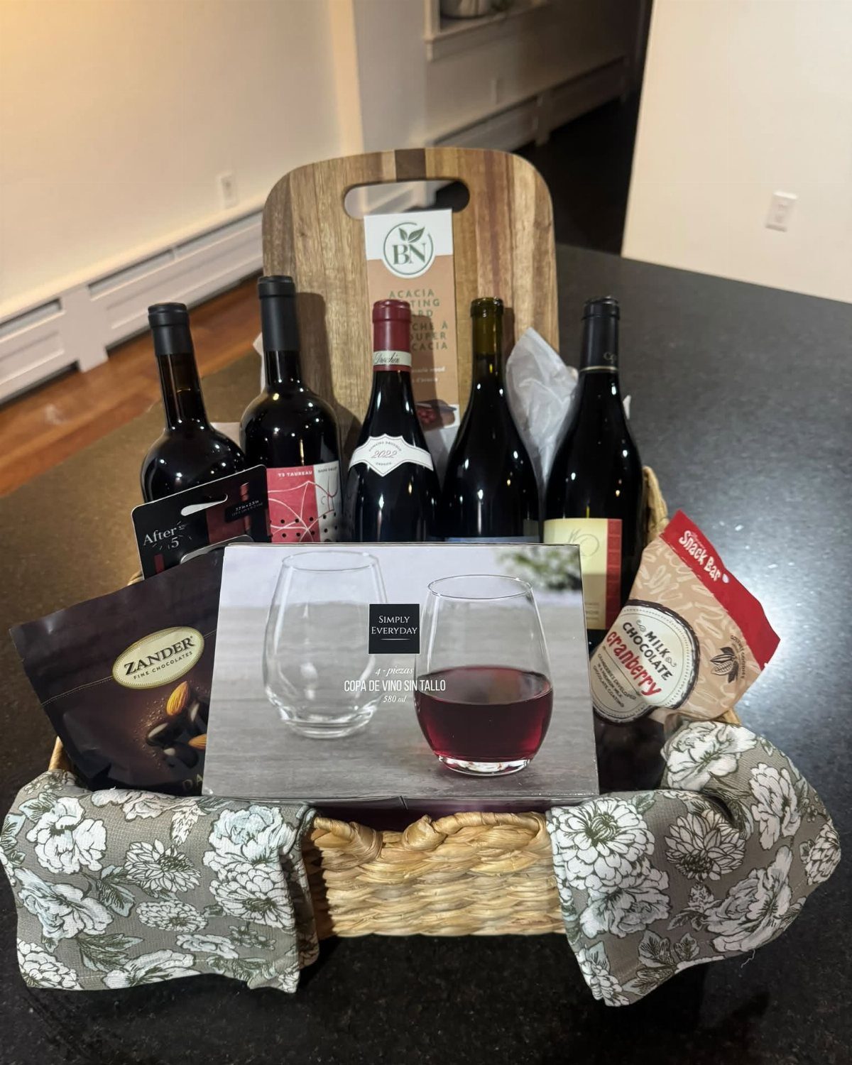 Wine gift basket with red wine bottles, glasses, and snacks on a counter